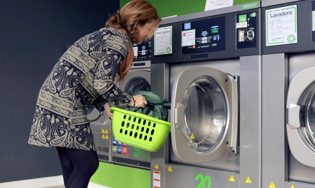 Mulher segurando cesta de roupas em frente a uma maquina de lavar roupas. Como montar uma lavanderia.